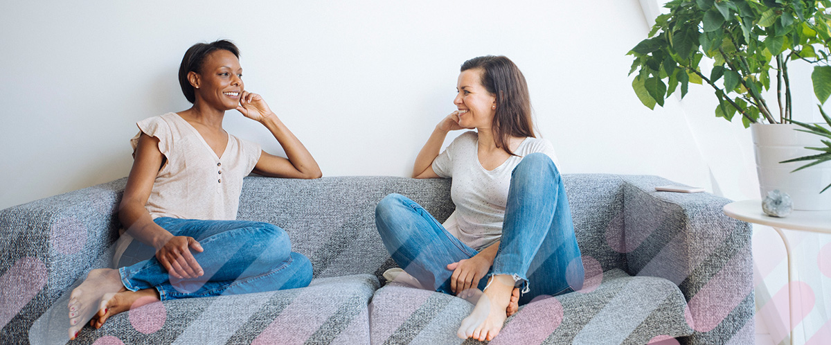 Two women sit facing one another on a couch