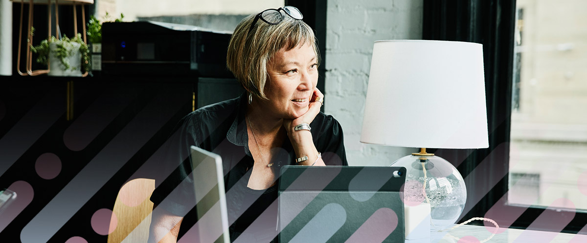 A woman gazes out a window while researching breast cancer treatment on a laptop